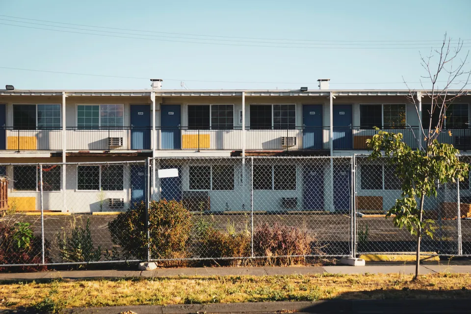 Closed, boarded-up two-story motel behind chain-link fence.
